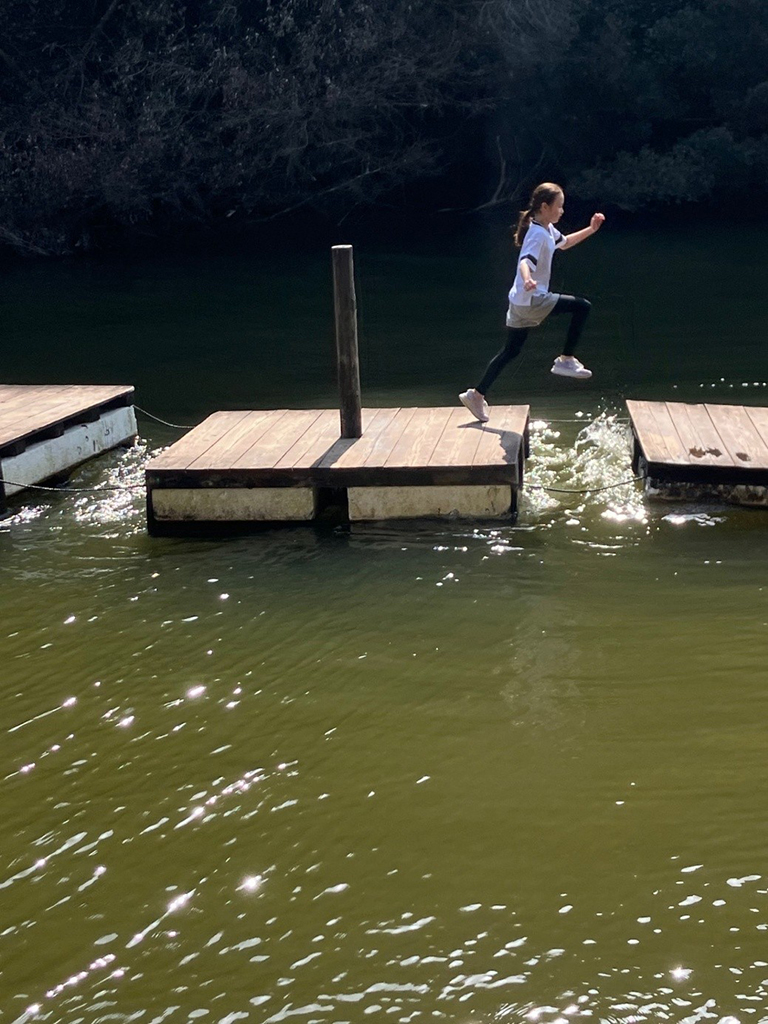 キラキラと光る水面の上、アスレチックの浮き島を元気にジャンプして飛び移る女の子